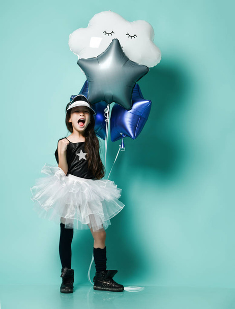 Cute little asian girl kid in fashion skirt holds metallic balloons for kids birthday and screams shouts sings on blue mint - Foto, Imagem