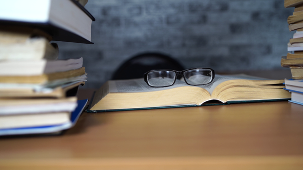 Buch und Brille auf dem Schreibtisch im Büro oder in der Bibliothek öffnen. Lernkonzepte - Filmmaterial, Video
