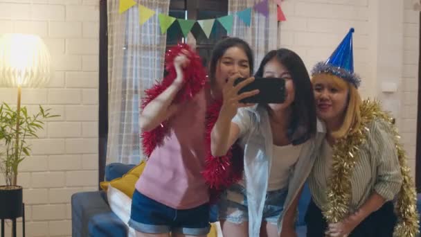 Group of Asian women party at home, female using mobile phone making vlog selfie to social media while funny dance together in living room in night. Young friend celebrate holiday concept. Slow motion - Footage, Video