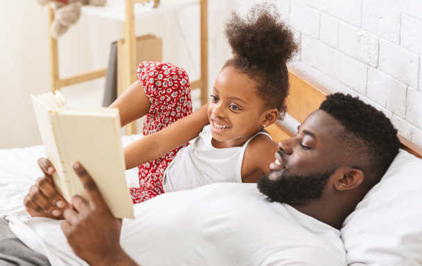おとぎ話を聞くかわいいアフリカの女の子、お父さんは彼の子供に本を読んで - 写真・画像