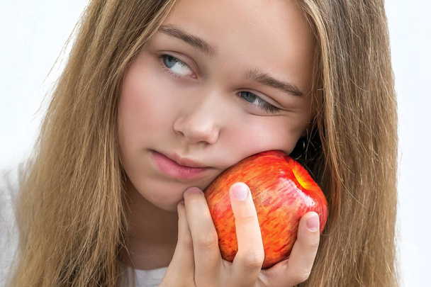  Dziewczyna w białej koszulce, trzymając Czerwone jabłko w rękach w pobliżu policzka  - Zdjęcie, obraz
