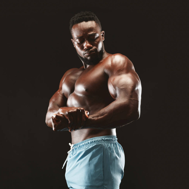 Αφρικανική bodybuilder δείχνοντας δικέφαλους σε μαύρο στούντιο - Φωτογραφία, εικόνα