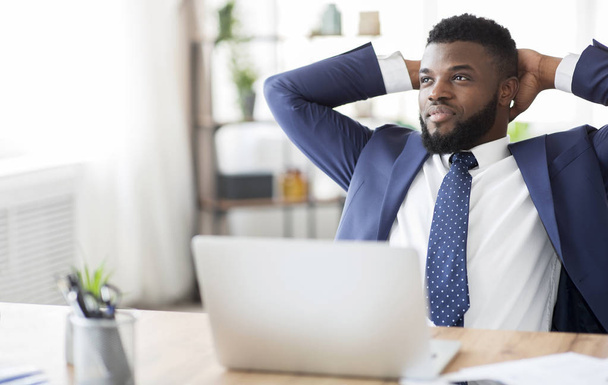 Zadowolony afrykański biznesmen siedzi z tyłu głowy w miejscu pracy - Zdjęcie, obraz