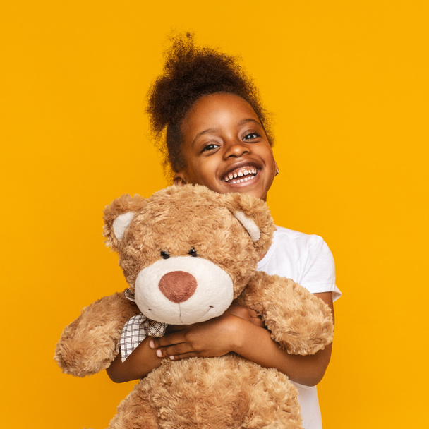 Lindo africano americano niño abrazando osito de peluche y sonriendo
 - Foto, imagen