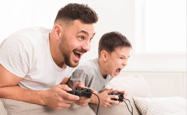 Emotionele vader en zoon spelen video game thuis, concurreren voor Win - Foto, afbeelding