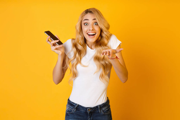 Счастливая удивленная женщина с мобильным телефоном на желтом фоне
 - Фото, изображение