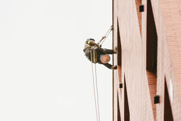 Ζωγράφος σκαρφαλωμένο κρέμονται στους τοίχους ενός κτιρίου με σχοινιά. - Φωτογραφία, εικόνα