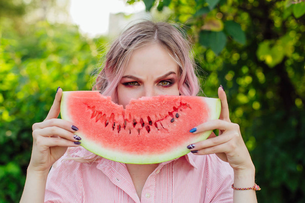 Beautiful young woman with pink hair holding juicy watermelon close to the face - Zdjęcie, obraz