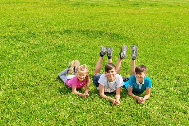 子供の男の子と女の子は公園の緑の草原の草の上に横たわっています。夏のコンセプト、新鮮な空気の中で子供のゲーム. - 写真・画像