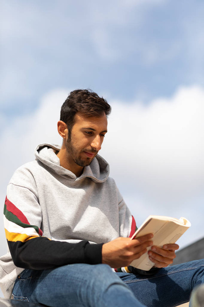 Young Bearded Man Reading A Book Sitting In A Park During The Morning. - Photo, Image
