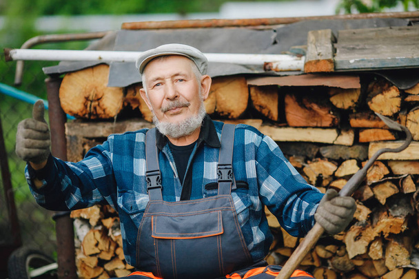 Senior lächelnder Mann schärft Werkzeug für die Bearbeitung von Ackerboden. Landwirtschaftskonzept - Foto, Bild