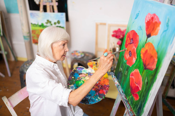 Blonde-haired woman painting red poppies on canvas - Fotoğraf, Görsel