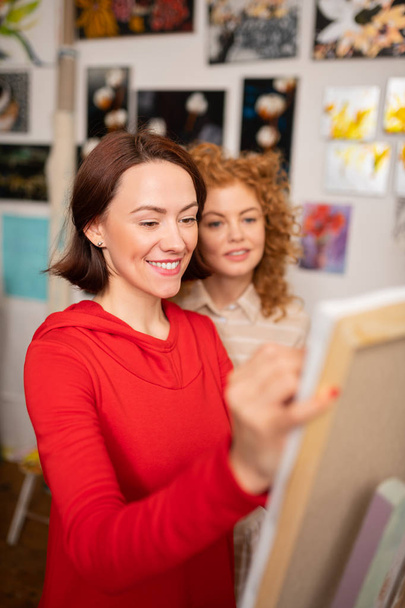 Jovem professora de arte sorrindo enquanto se aproxima de seu aluno
 - Foto, Imagem