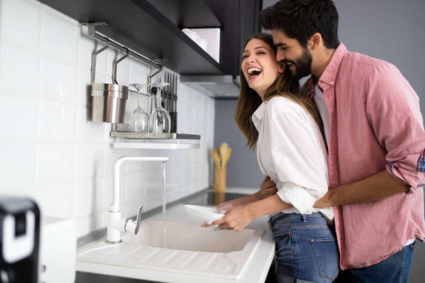 Young happy couple is washing dishes and hugging smiling - Фото, зображення