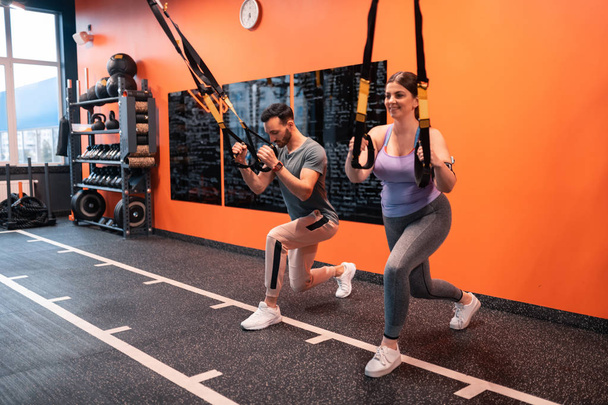 Trainer and his client lunging forward holding TRX straps - Photo, Image
