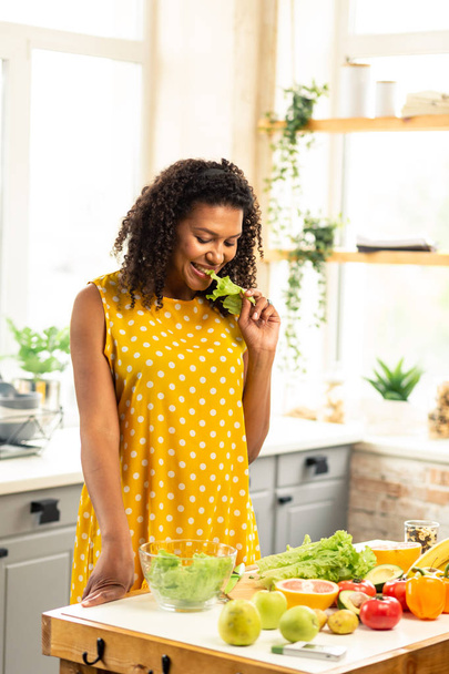 Happy pregnant woman eating lettuce in her kitchen. - Foto, afbeelding