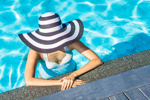 Seyahat için yüzme havuzunda şapkalı güzel genç Asyalı kadın - Fotoğraf, Görsel