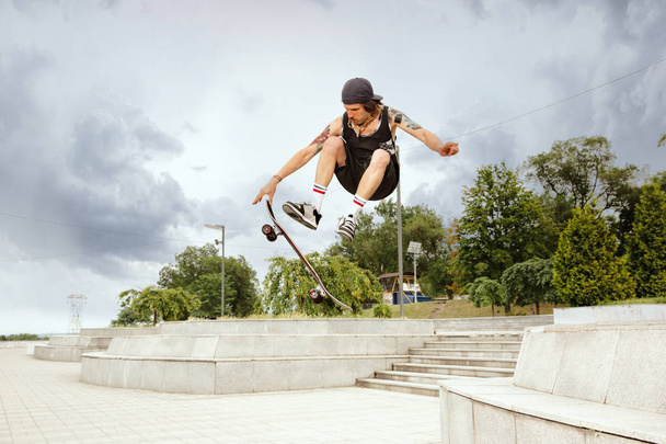 Skateboarder doing a trick at the citys street in cloudly day - Foto, imagen