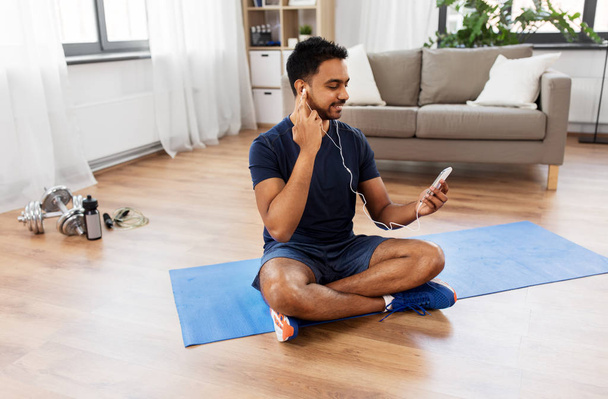 indian man with smartphone on exercise mat at home - Valokuva, kuva
