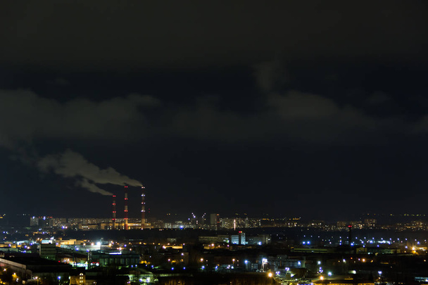 skyline de la ciudad por la noche.Vista nocturna de un barrio con bloques de apartamentos de poca altura iluminado luces de ventana. Tubos de humo de la central térmica
 - Foto, imagen