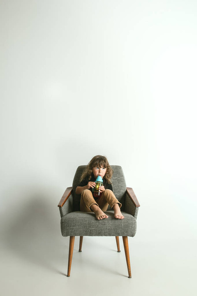 Little child sitting and playing in armchair on white studio background - Foto, Imagen
