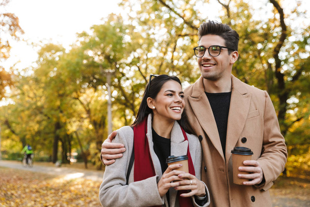 Portrait of caucasian couple drinking takeaway coffee from paper cups while walking in autumn park - Foto, immagini