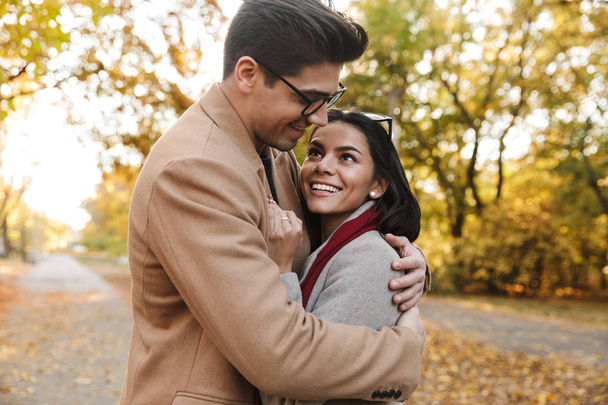Image of charming brunette couple smiling and hugging in autumn park - 写真・画像