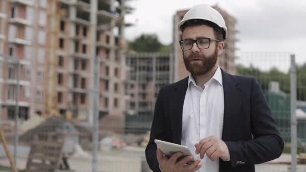 Architect man wearing business suit walking with tablet on the construction site and analyzing scheme project plan. Outside, slow motion. - Metraje, vídeo