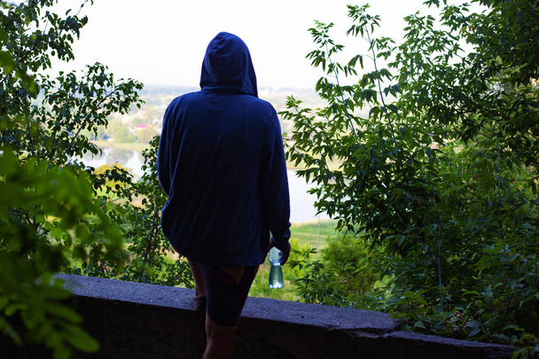 der Typ mit der Kapuze denkt über Selbstmord nach, ein junger Mann steht mit einem Fuß auf einer Stufe nahe einer Klippe, Selbstmordgedanke - Foto, Bild