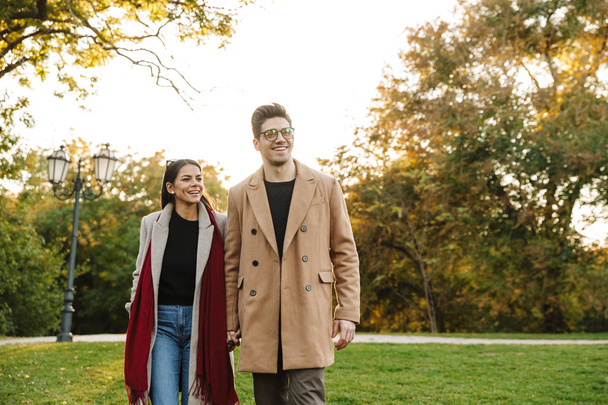Portrait of young casual couple smiling at camera and walking in autumn park - Fotó, kép