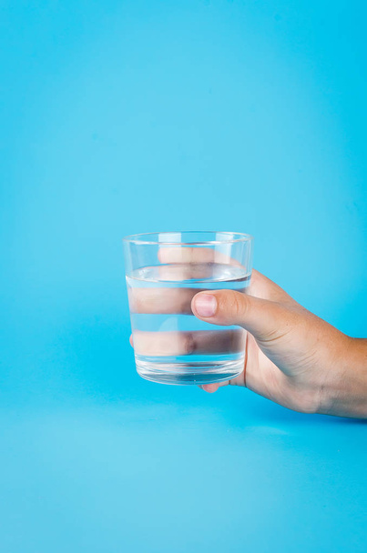 glass of water in hand on blue - Foto, imagen