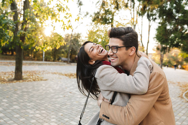 Portrait of happy joyful couple laughing and hugging each other while walking in autumn park - Photo, Image