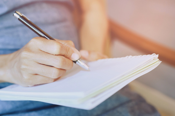 κοντινό χέρι γυναίκα γράφουν σημειωματάριο κάτω κόστος στο βιβλίο στον καναπέ - Φωτογραφία, εικόνα