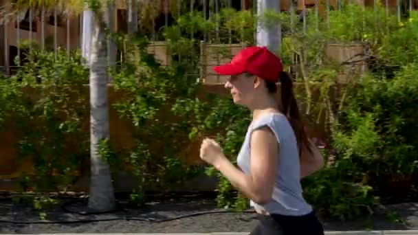 Kadın sokakta palmiye ağaçları arasında koşuyor. Sağlıklı aktif yaşam tarzı. Yavaş hareket - Video, Çekim