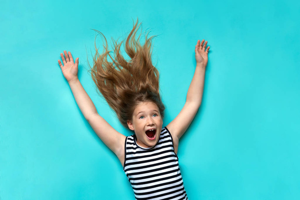Happy child laying on blue backdrop with hands up - Фото, зображення