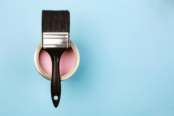 Brush on open can of pink paint on blue pastel background. - Foto, Imagen