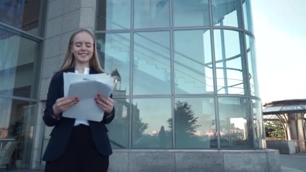 young business women black suit look at paper documents, smile and throw them in to the air. Modern, contemporary glass building on background - Video