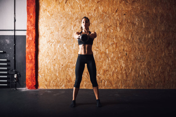Молодая женщина делает упражнения в помещении с гирями
 - Фото, изображение