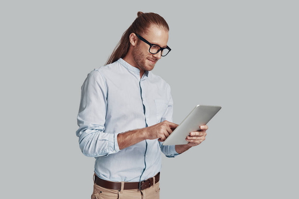 Alla ricerca di nuove idee. Bello giovane uomo che lavora con il computer portatile e sorridente mentre in piedi su sfondo grigio
 - Foto, immagini