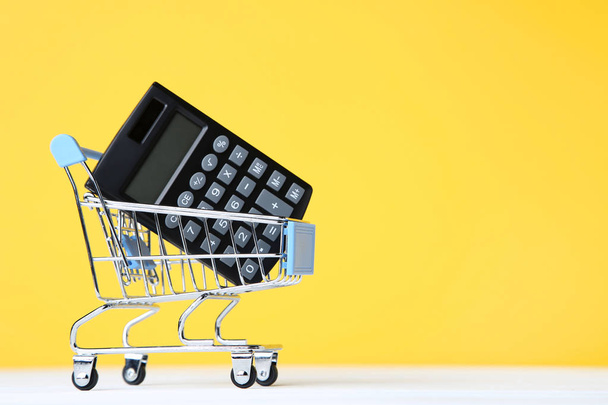Small shopping cart with calculator on yellow background - Photo, Image