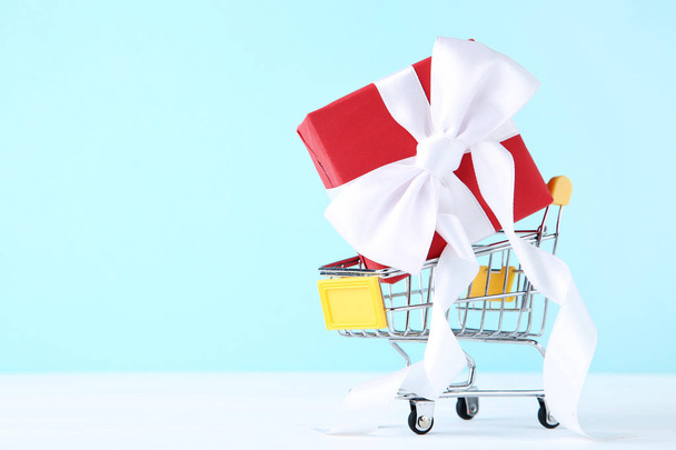 Small shopping cart with gift box on blue background - Φωτογραφία, εικόνα