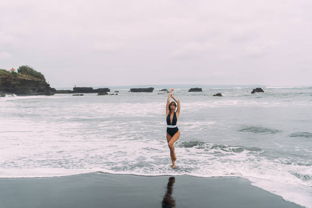 Happy girl in dark swimsuit relaxes at beach with beautiful waves on background - Foto, Bild