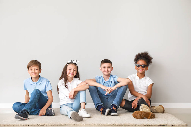 Niños con estilo en jeans sentados cerca de la pared de luz
 - Foto, imagen