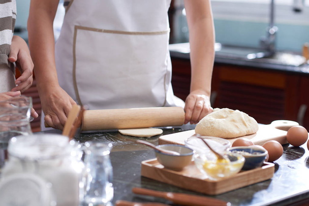 Hands of woman rolling out cookie dough on kitchen table - Fotó, kép