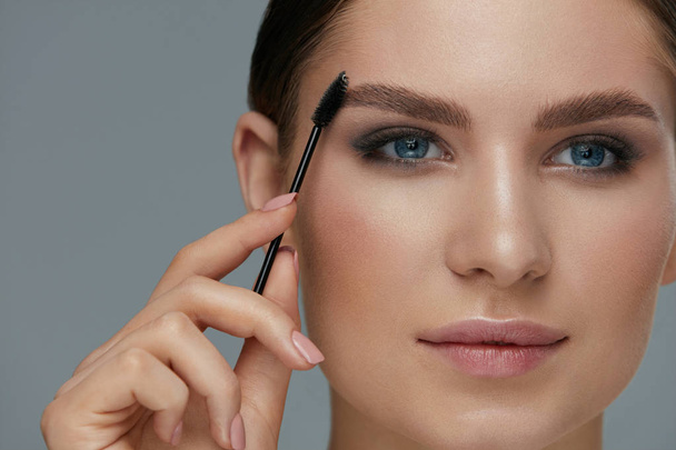 Eyebrow makeup. Woman brushing brows with gel brush closeup - Foto, afbeelding