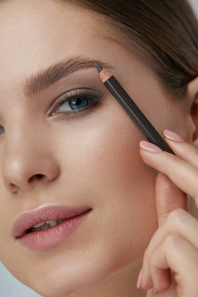 Eyebrow makeup. Beauty model shaping brows with brow pencil - 写真・画像