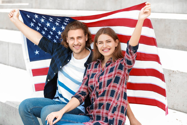 Ευτυχισμένο νεαρό ζευγάρι με τις ΗΠΑ σημαία σε εξωτερικούς χώρους. Εορτασμός της ημέρας ανεξαρτησίας - Φωτογραφία, εικόνα