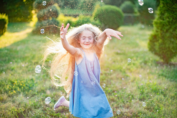 Criança a rodopiar, dança a brincar no prado. Menina se divertindo com bolhas. bonito pouco longhair loira menina dançando com sabão bolhas no por do sol parque - Foto, Imagem