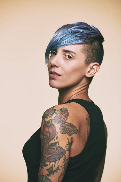 Κομψή γυναίκα με τατουάζ στα χέρια της γυρίζοντας πίσω και κοιτάζοντας την κάμερα - Φωτογραφία, εικόνα