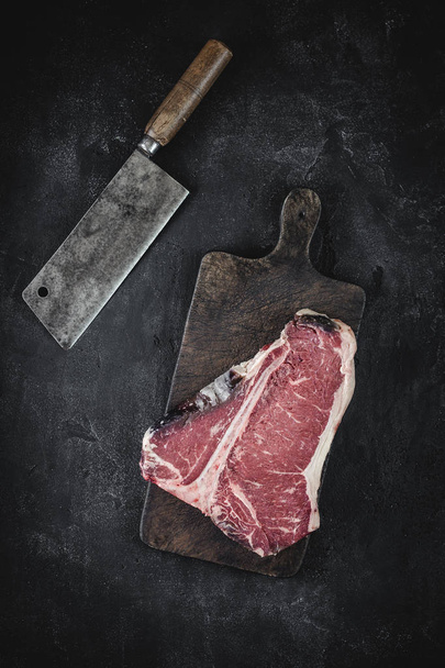 Nyers száraz év T-bone steak a Vintage vágódeszka a hús Cleaver - Fotó, kép